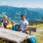 Schmitten Wandern Familie A family sitting on a mountain, on a bench.