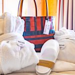 Latini_Zimmer_Bademantel_Badetasche A bed with a bag, bathrobes and a pair of slippers.