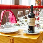 Latini_Restaurant_Impression_1 Eine große Sitzbank mit Tischen, Weingläsern und einer Weinflasche.