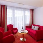 Ein Raum mit einer Fensterfront und zwei Sesseln, einem Sofa sowie einem kleinen Tisch.